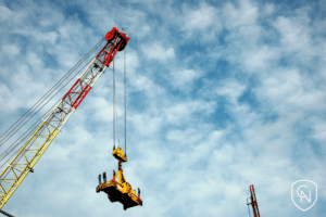 In Manhattan, a yellow crane holding a large magnet with a cloudy blue sky backdrop